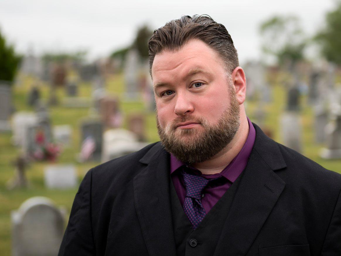 Tim Weisberg pictured in a cemetery wearing a black suit.